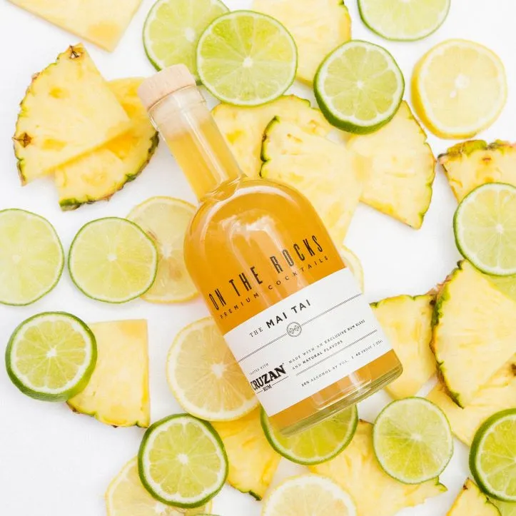 A bottle of On The Rocks Mai Tai lying on pineapple and lime slices