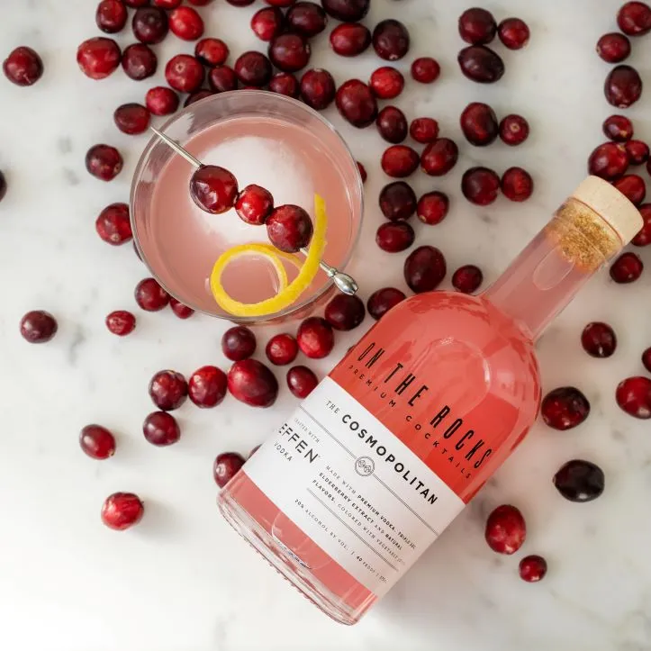 A bottle of On The Rocks Cosmopolitan lying next to a cocktail glass