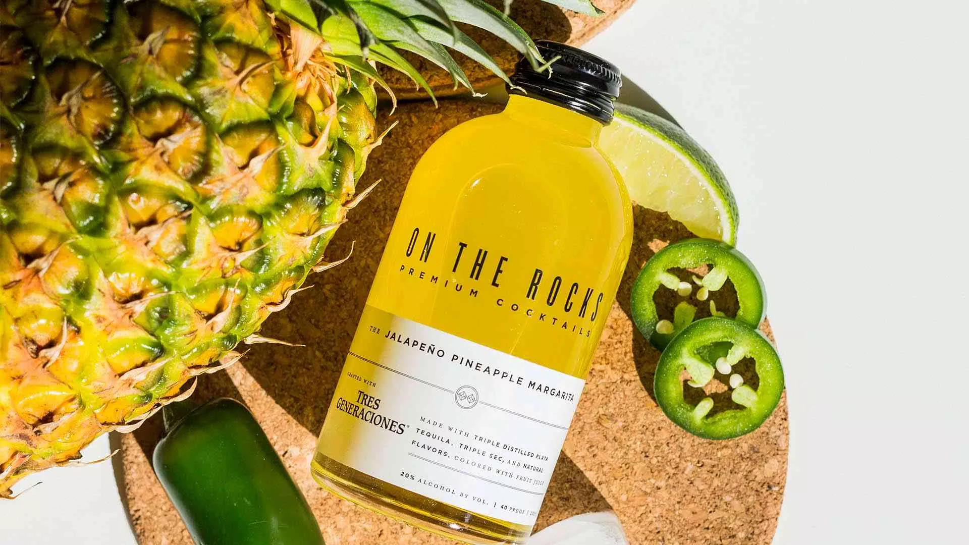 OTR Pineapple Jalapeno Margarita bottle lying next to some jalapenos, a lime and a pineapple