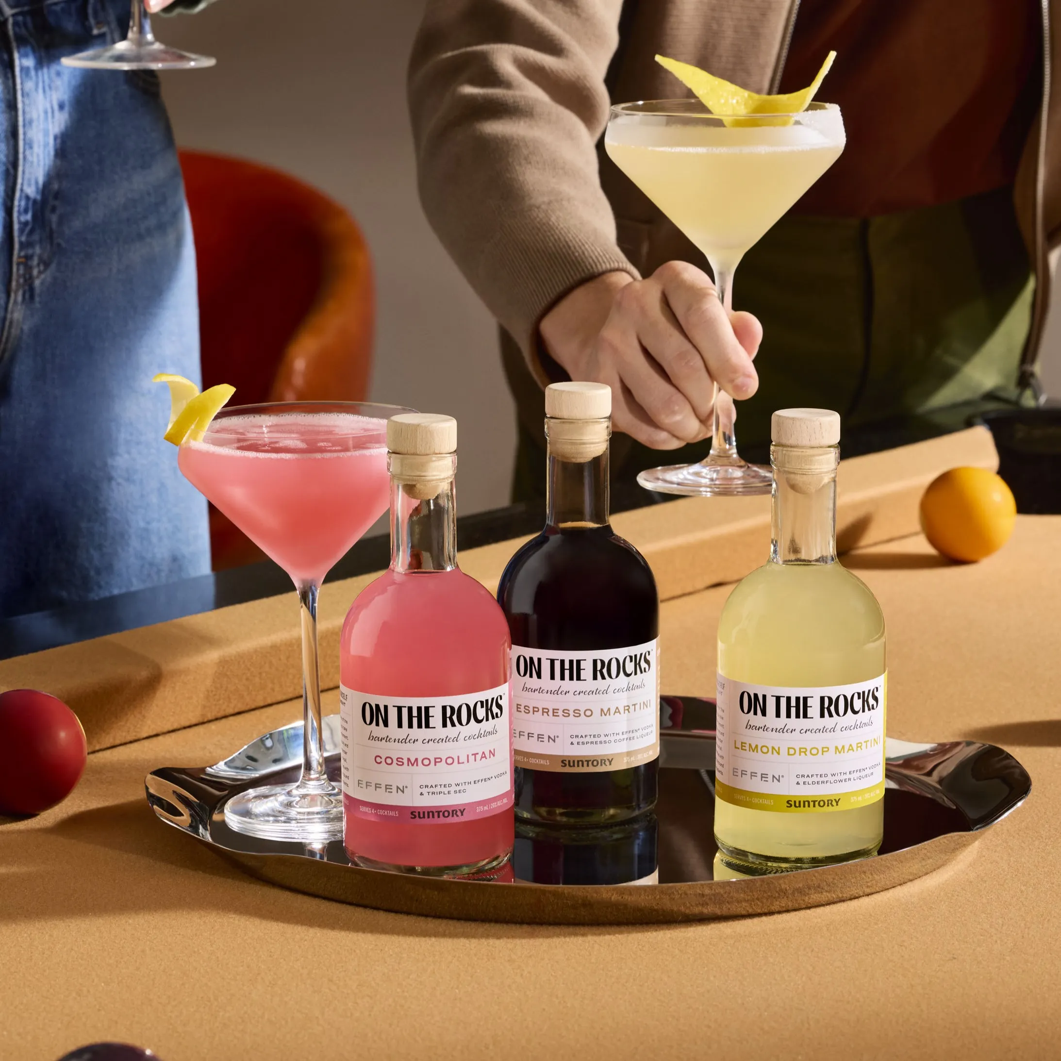 A tray with three "On The Rocks" cocktail bottles (Cosmopolitan, Espresso Martini, Lemon Drop Martini) on a pool table.